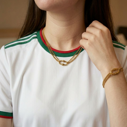 Close-up of a person wearing a white shirt with green and red trim, gold necklace, and bracelet.