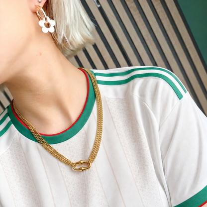 Person wearing a white shirt with green and red trim, gold chain necklace, and floral earrings.