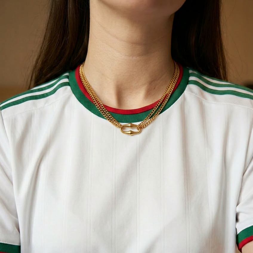 Person wearing a white shirt with green and red accents and gold necklaces.
