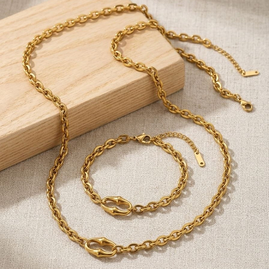 Gold chain necklace and bracelet set on a wooden block with a beige fabric background