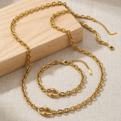 Gold chain necklace and bracelet set on a wooden block with a beige fabric background
