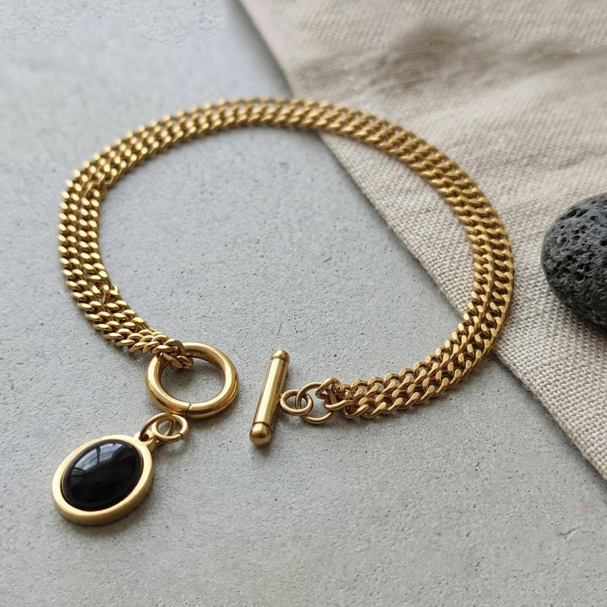 Gold chain bracelet with a black pendant on a light surface