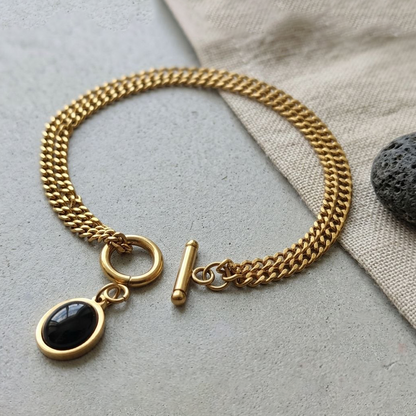 Gold chain bracelet with a black pendant on a light surface