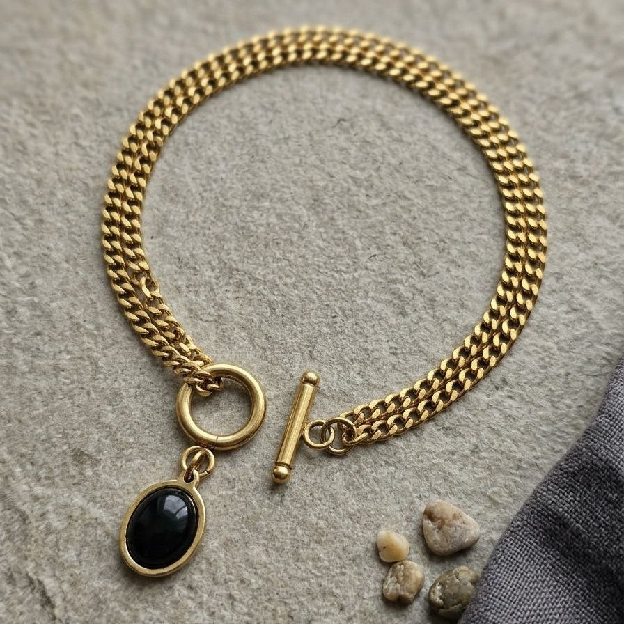 Gold chain bracelet with a black stone charm on a stone surface