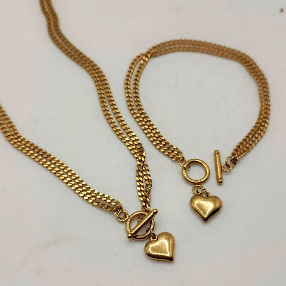 A gold-toned necklace and matching bracelet set with heart charms and toggle closures, displayed on a plain light background.